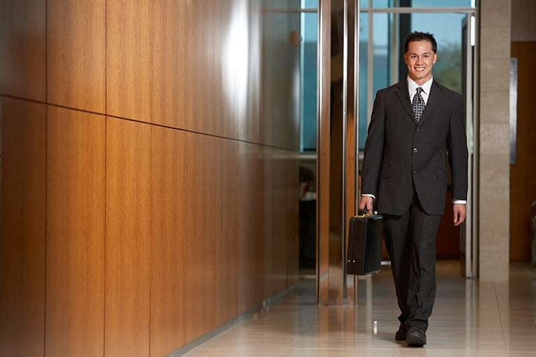 Man in a suit walking in a hallway holding a briefcase.