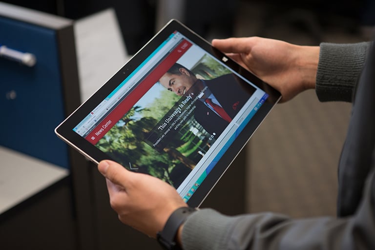 Hands holding a tablet that shows the U-N-L-V News Center on the screen.